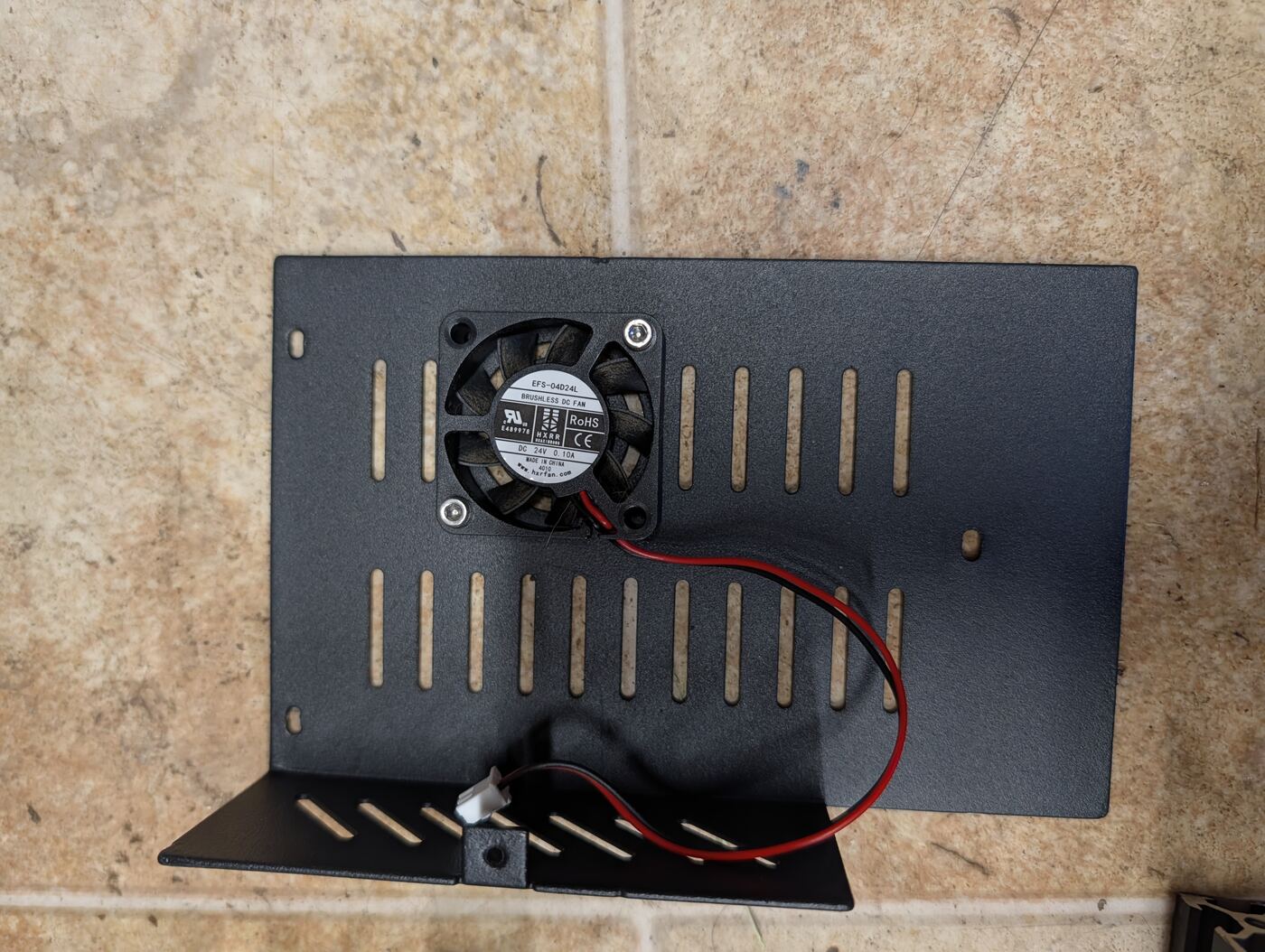 A salvaged metal bracket with a small cooling fan mounted, from a donor 3D printer mainboard enclosure